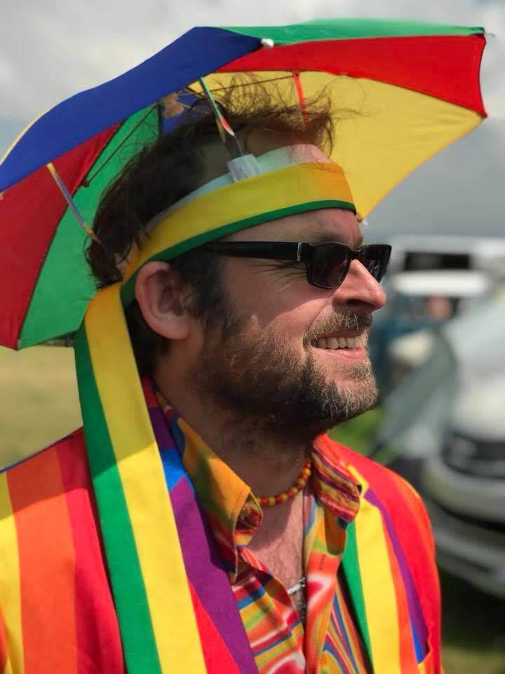 tom dressed up in some rainbow colours with a umbrella as a hat