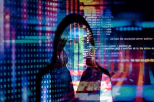 コンピューター コードの大きな投影画像の前に立つ女性。 彼女の顔と胴体にコードが投影されたさまざまな色とライトがあります。