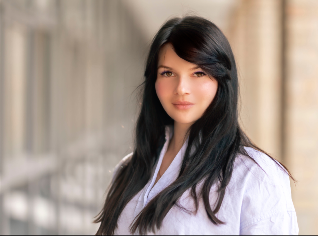 Sabina Auhunas is a woman with long black hair and brown eyes wearing a white shirt. 