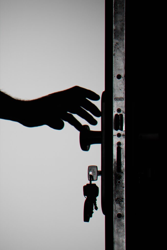 Uma imagem em preto e branco da lateral de uma abertura de porta. Uma mão está alcançando a maçaneta e as chaves estão na fechadura. Esta imagem representa a ideia de segurança de pesquisa e abertura.