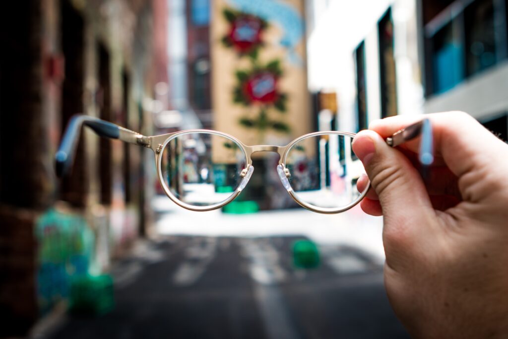 A blurry view in a city with a hand holding glasses in the middle of the frame representing accessibility.
