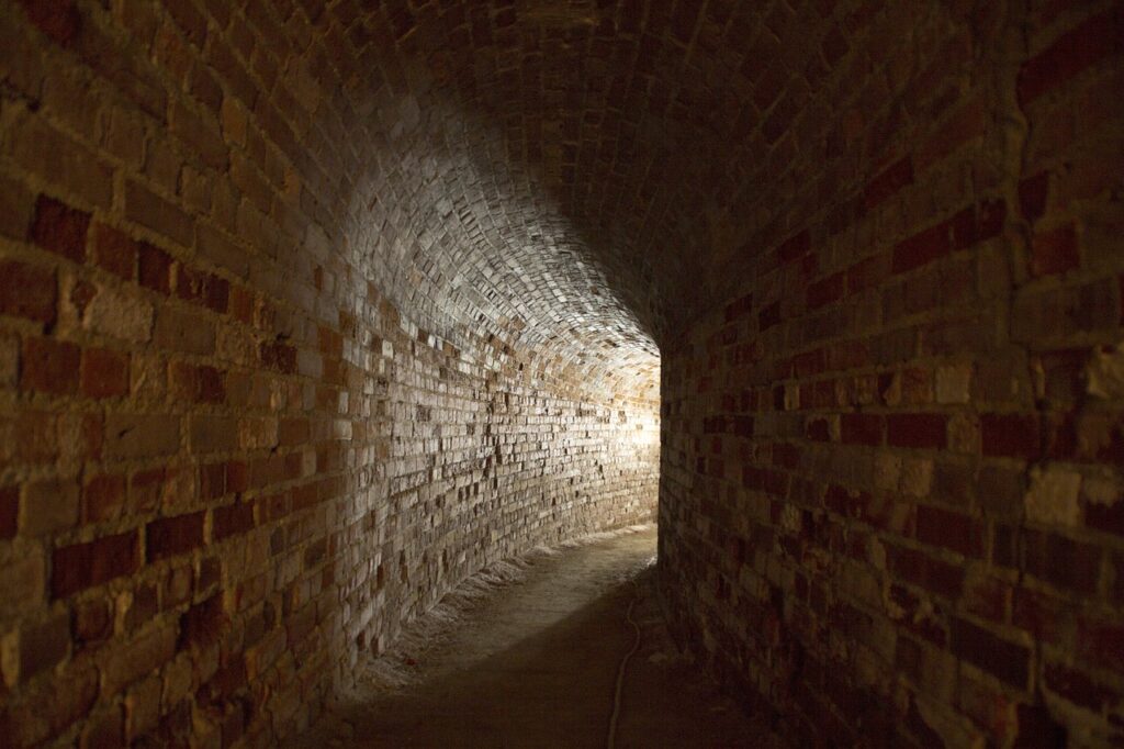 dark brick curved corridor with a light shining from the other end. 